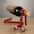 Wine bottle balanced on a red metal ribbon-shaped holder on wooden table