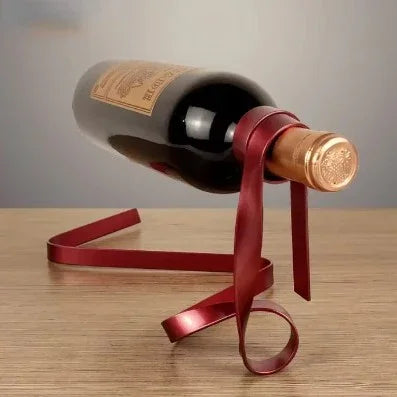 Wine bottle balanced on a red metal ribbon-shaped holder on wooden table